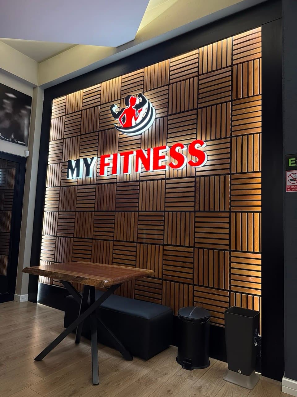 The backlit My Fitness logo wall above a wooden table in the entrance lounge