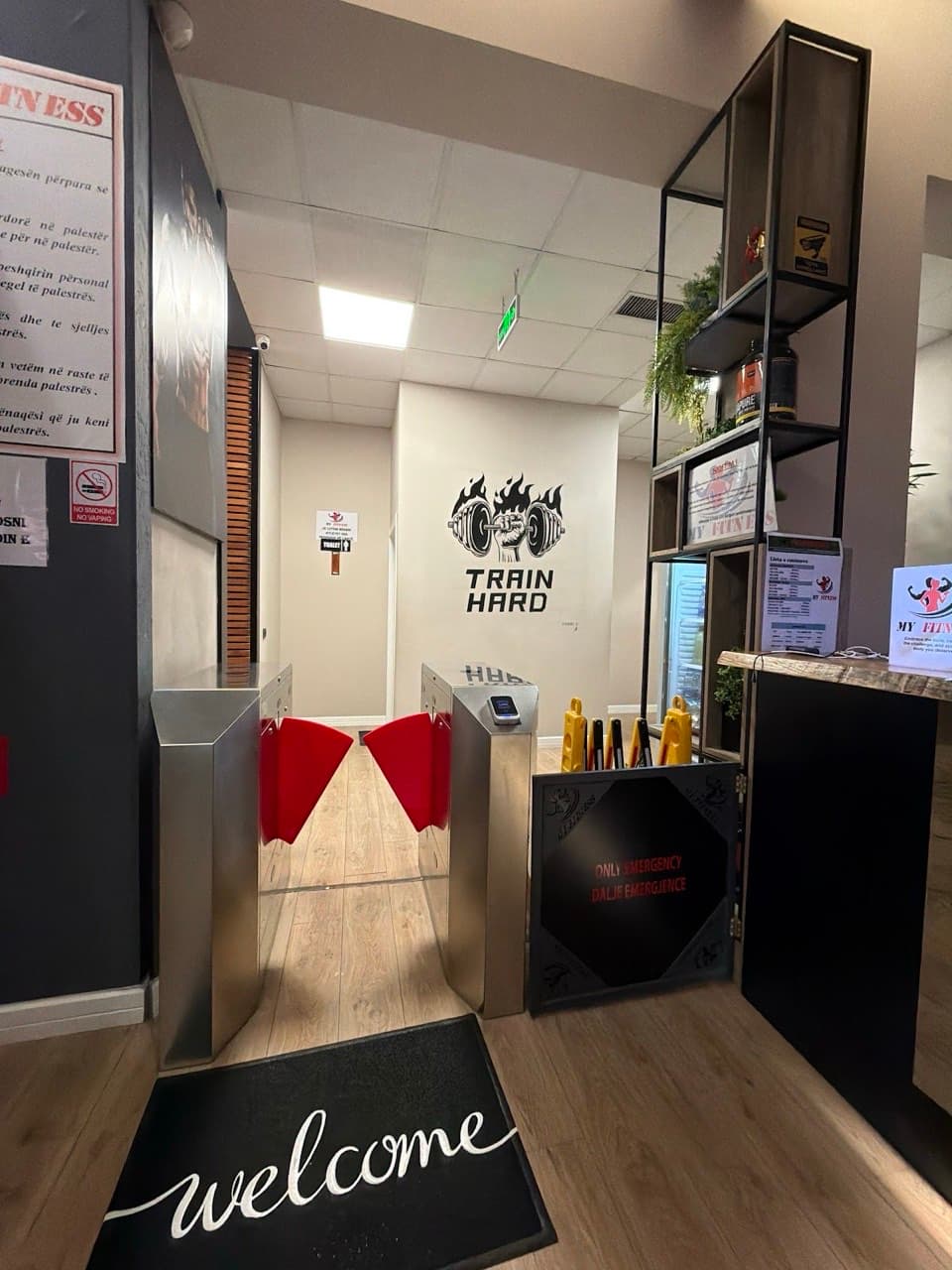 Entry turnstiles beneath a 'Train Hard' wall graphic at the My Fitness reception welcome mat