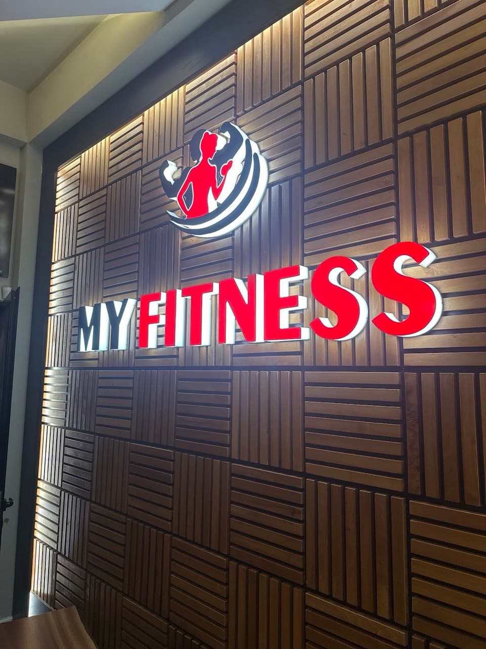 A close-up of the backlit My Fitness logo on the wood-panelled entrance wall