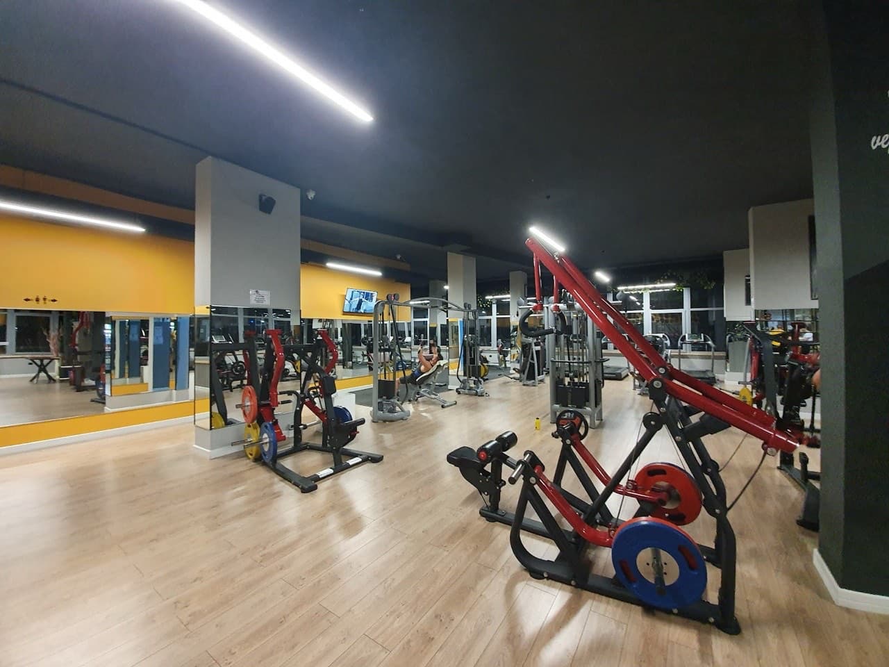 Red and black resistance and leg press machines across the training floor under warm lighting