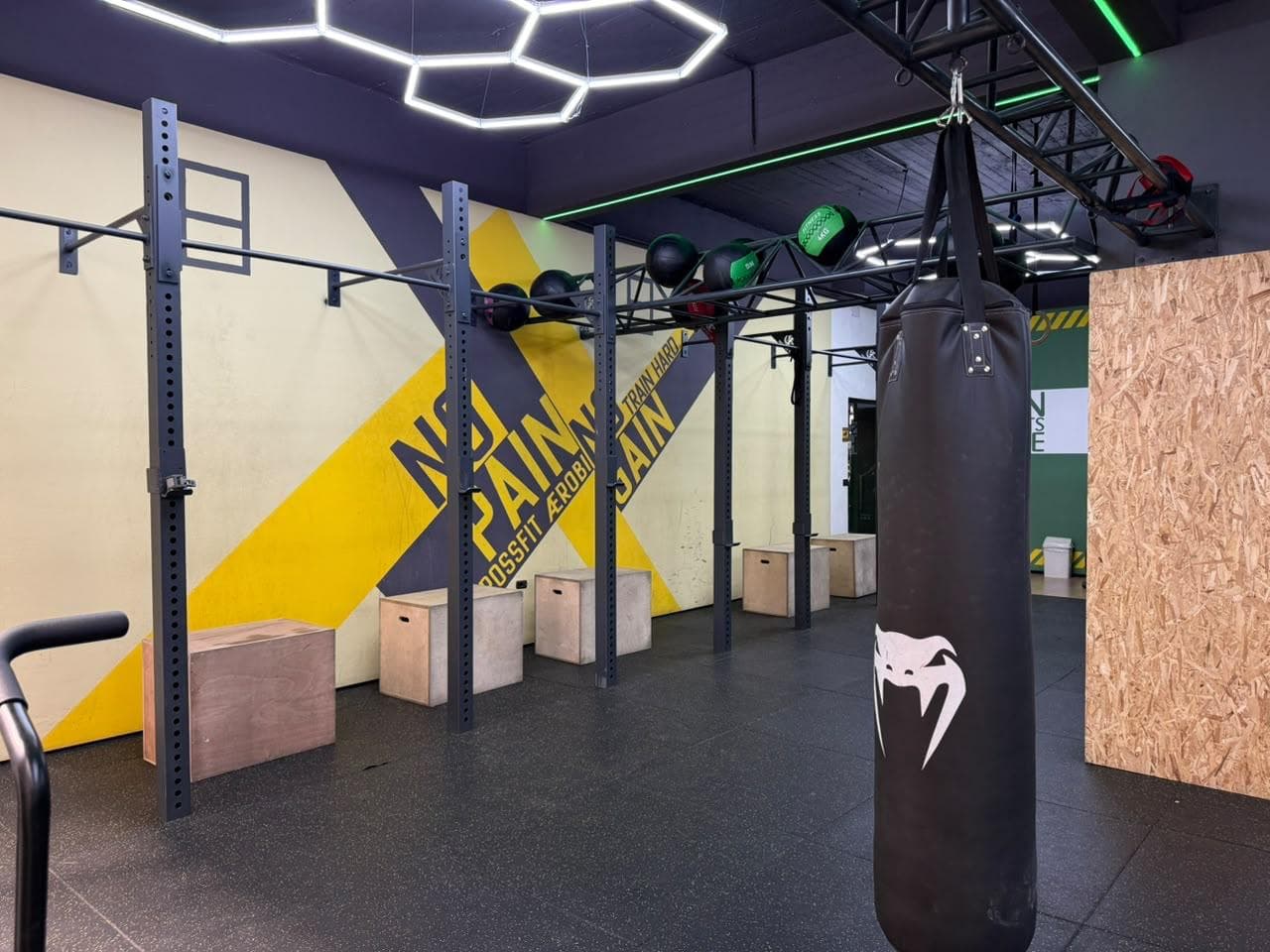 A steel training rig hung with medicine balls beside a punching bag and plyo boxes at My Fitness